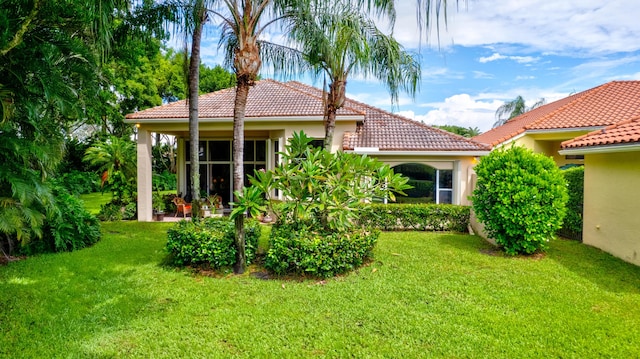 back of property featuring a tile roof, a lawn, and stucco siding