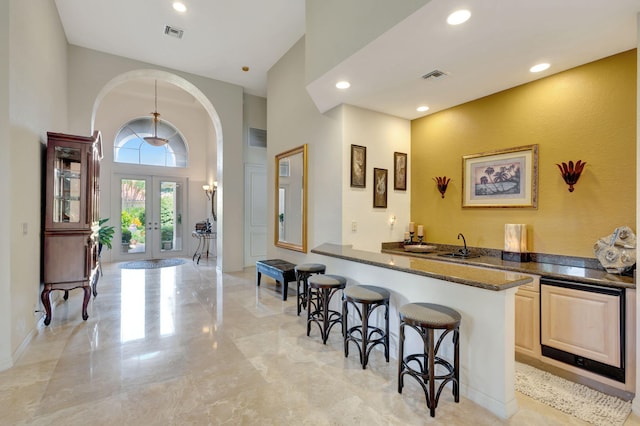 bar featuring french doors, dark stone counters, and a high ceiling