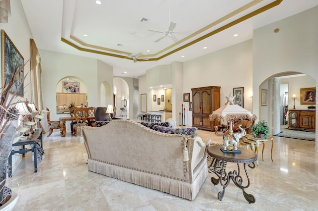 living room with a tray ceiling, a high ceiling, and ceiling fan