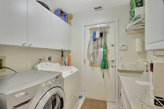 clothes washing area with washing machine and dryer, light tile patterned floors, a textured ceiling, cabinets, and sink