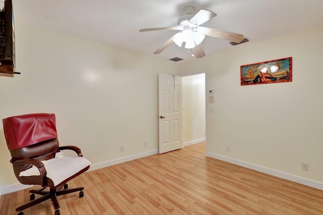 living area featuring light hardwood / wood-style flooring, ceiling fan, and a textured ceiling