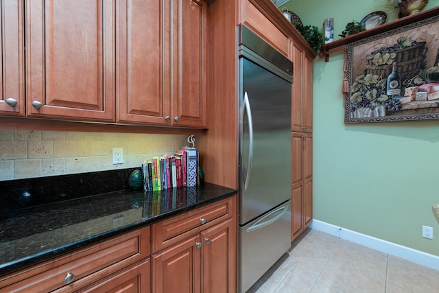 kitchen featuring light tile patterned flooring, stainless steel built in refrigerator, backsplash, and dark stone counters