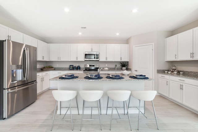 kitchen featuring stainless steel appliances, light stone counters, white cabinetry, and a kitchen island