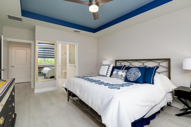 bedroom with a raised ceiling, ensuite bath, and ceiling fan