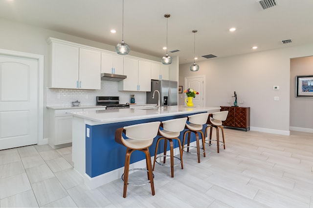 kitchen featuring a kitchen island with sink, a breakfast bar area, white cabinets, appliances with stainless steel finishes, and decorative light fixtures