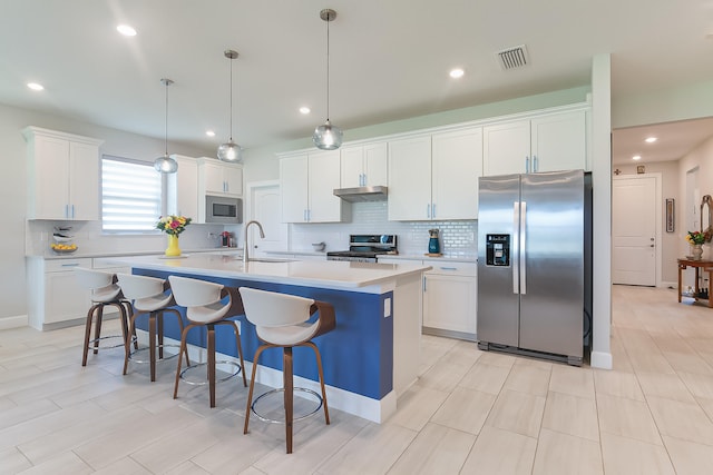 kitchen featuring a kitchen island with sink, sink, white cabinetry, hanging light fixtures, and stainless steel appliances