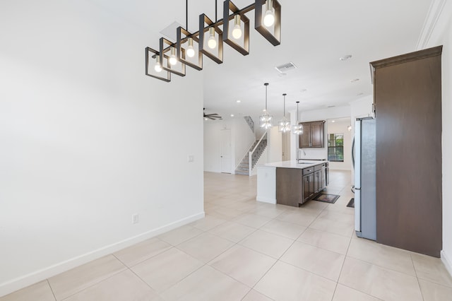 kitchen featuring stainless steel refrigerator, light tile patterned floors, dark brown cabinetry, decorative light fixtures, and a center island with sink