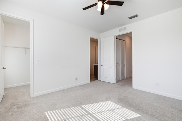 unfurnished bedroom with ceiling fan, a closet, light carpet, and a spacious closet