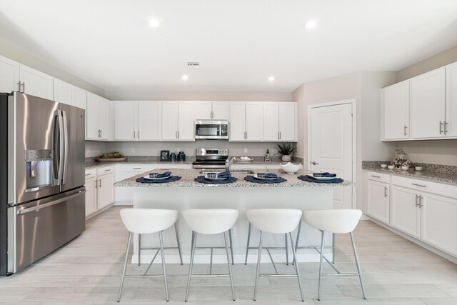 kitchen with light stone countertops, stainless steel appliances, white cabinetry, and a center island