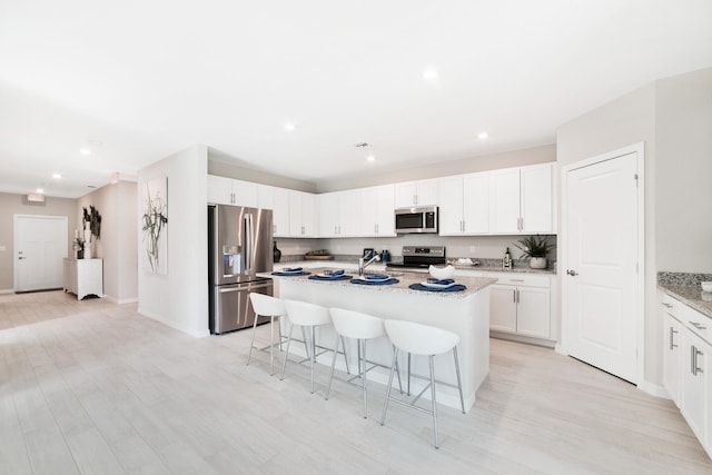 kitchen with light wood-type flooring, light stone counters, a kitchen island with sink, white cabinetry, and appliances with stainless steel finishes