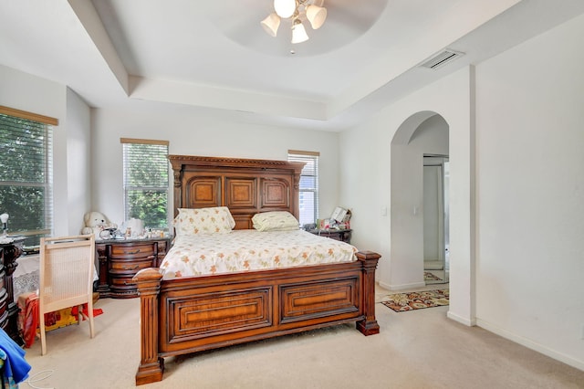 bedroom featuring visible vents, a raised ceiling, arched walkways, and light colored carpet