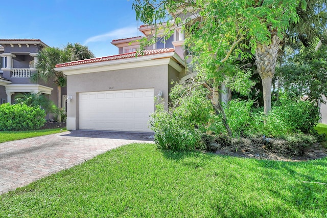 mediterranean / spanish-style home featuring a front yard, a tiled roof, an attached garage, stucco siding, and decorative driveway