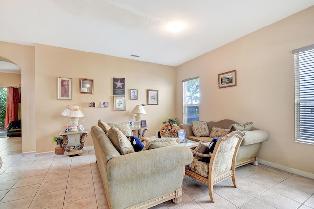 living area featuring arched walkways, light tile patterned floors, baseboards, and visible vents