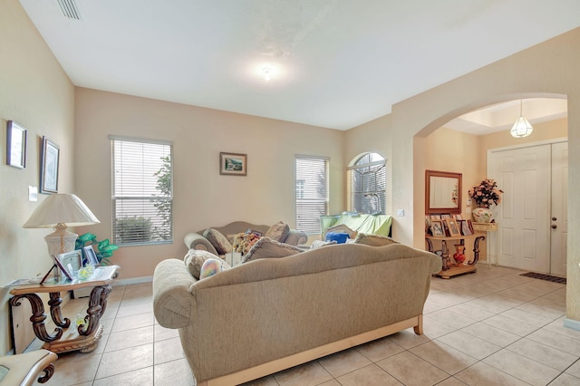 living room featuring a wealth of natural light, arched walkways, light tile patterned floors, and visible vents