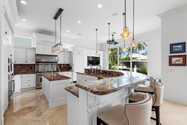 kitchen with an island with sink, stainless steel appliances, backsplash, decorative light fixtures, and white cabinetry