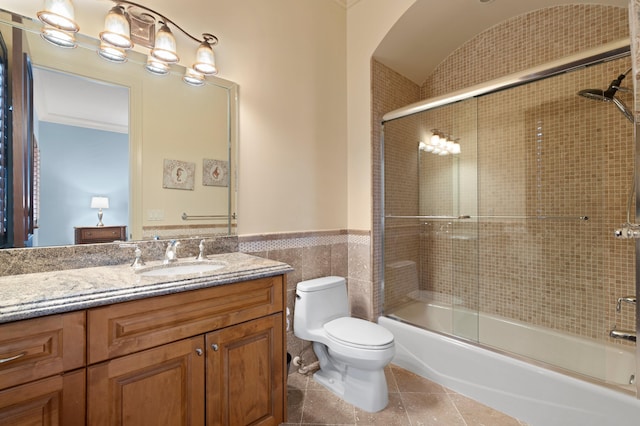 full bathroom with combined bath / shower with glass door, toilet, tile walls, vanity, and tile patterned flooring