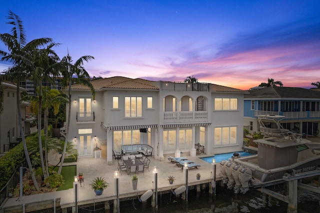 back house at dusk featuring a patio and a balcony