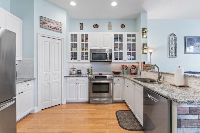 kitchen with appliances with stainless steel finishes, light wood-type flooring, sink, and white cabinetry