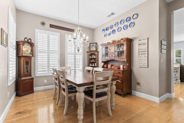 dining space featuring a textured ceiling, a healthy amount of sunlight, light hardwood / wood-style floors, and an inviting chandelier