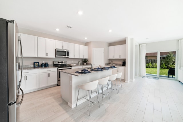 kitchen with an island with sink, white cabinetry, appliances with stainless steel finishes, and a breakfast bar area