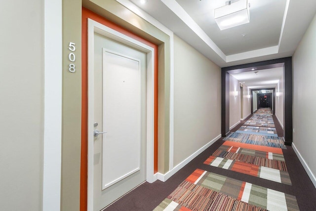 hallway with a raised ceiling and dark carpet