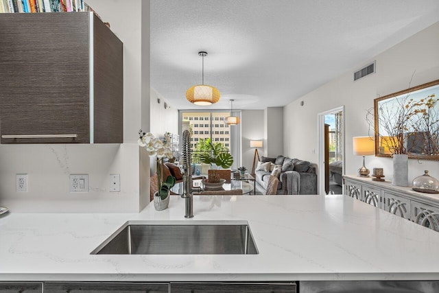 kitchen with a wealth of natural light, a textured ceiling, hanging light fixtures, and sink