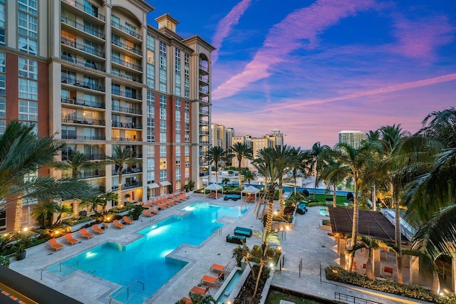 pool at dusk featuring a patio area and a hot tub