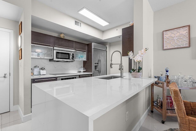 kitchen with light stone counters, sink, appliances with stainless steel finishes, light tile patterned floors, and dark brown cabinetry