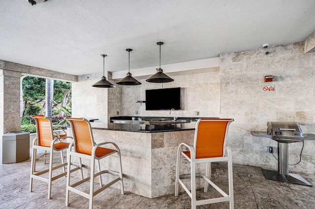 kitchen with pendant lighting, a textured ceiling, tile walls, and sink