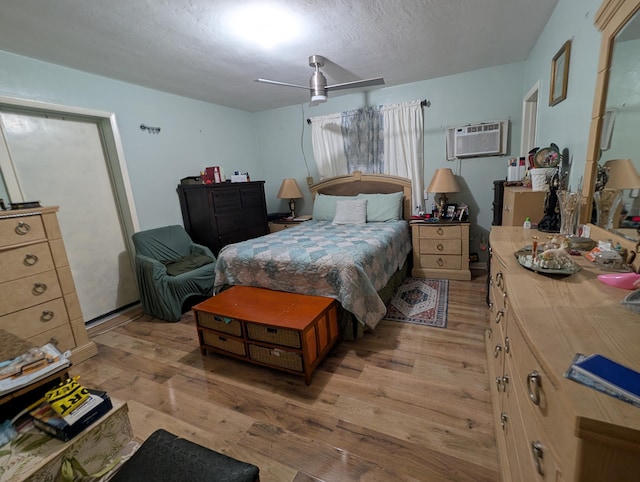 bedroom with ceiling fan, light hardwood / wood-style floors, a wall unit AC, and a textured ceiling