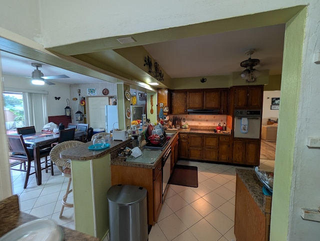 kitchen with light tile patterned floors, oven, kitchen peninsula, and a kitchen bar