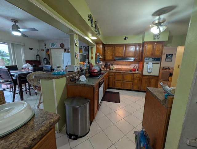 kitchen with light tile patterned floors, ceiling fan, dishwasher, kitchen peninsula, and oven