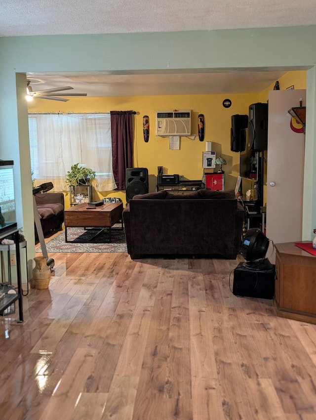 living room featuring ceiling fan, an AC wall unit, a textured ceiling, and light hardwood / wood-style flooring