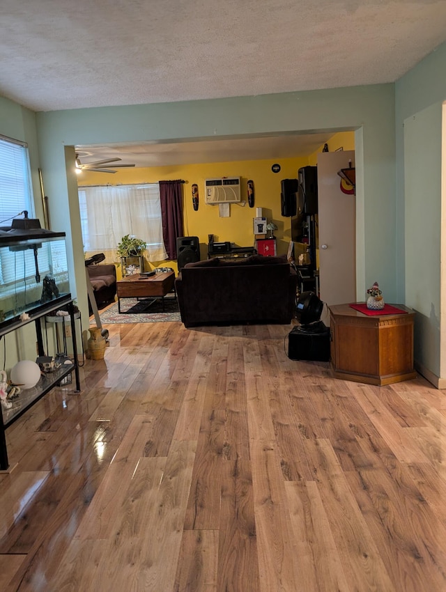 living room featuring an AC wall unit, a textured ceiling, and light hardwood / wood-style flooring