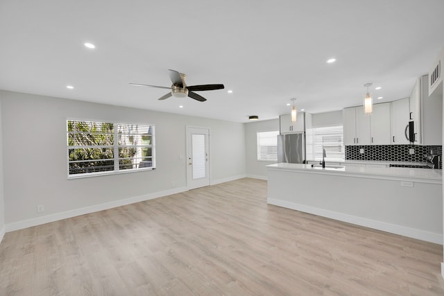 unfurnished living room with light wood-type flooring, ceiling fan, plenty of natural light, and sink