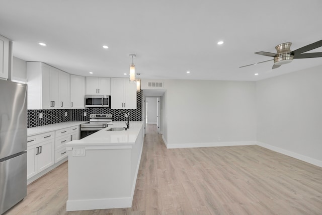 kitchen with pendant lighting, stainless steel appliances, white cabinets, and light wood-type flooring