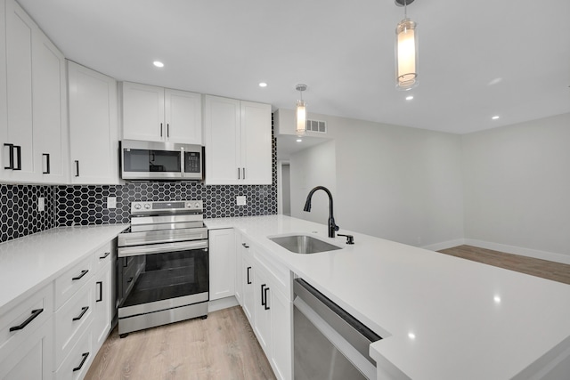 kitchen with light hardwood / wood-style floors, sink, white cabinets, hanging light fixtures, and appliances with stainless steel finishes