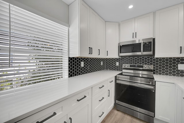 kitchen with white cabinets, light wood-type flooring, stainless steel appliances, and backsplash