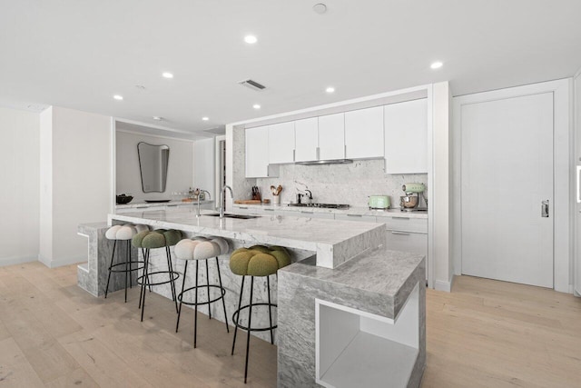 kitchen featuring white cabinetry, a large island with sink, light hardwood / wood-style flooring, and sink