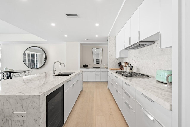 kitchen featuring wine cooler, a large island with sink, white cabinetry, light hardwood / wood-style flooring, and sink