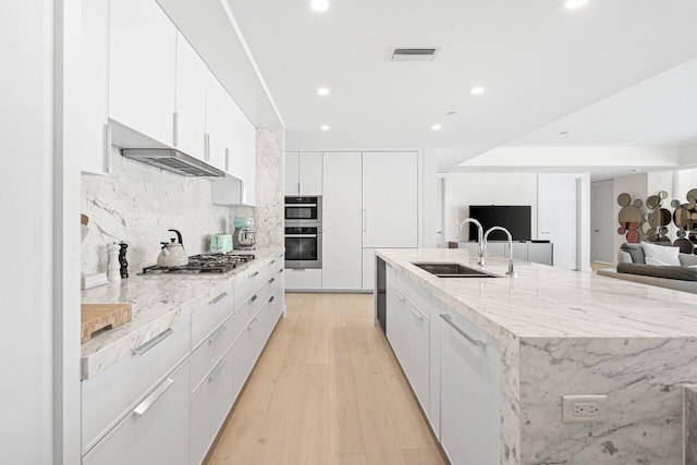 kitchen featuring a large island with sink, sink, white cabinetry, and light hardwood / wood-style flooring