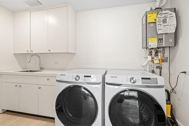 washroom with cabinets, water heater, washing machine and dryer, light hardwood / wood-style floors, and sink