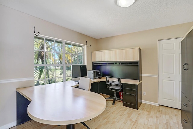 home office with a textured ceiling, light wood-type flooring, and baseboards