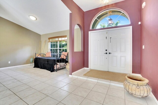 entrance foyer featuring vaulted ceiling, light tile patterned floors, and baseboards