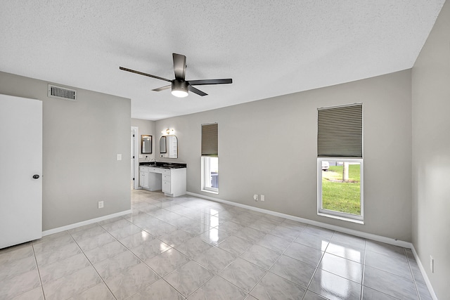 unfurnished living room with ceiling fan, a textured ceiling, and light tile patterned floors