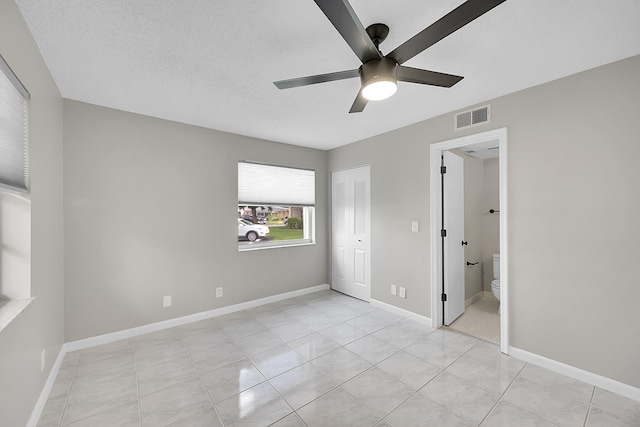 unfurnished bedroom with ceiling fan, light tile patterned flooring, a textured ceiling, a closet, and ensuite bath