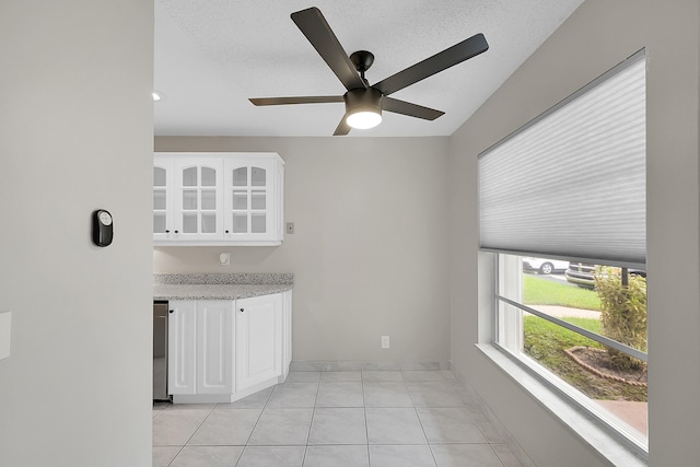 kitchen with ceiling fan, white cabinets, light tile patterned floors, a textured ceiling, and light stone countertops