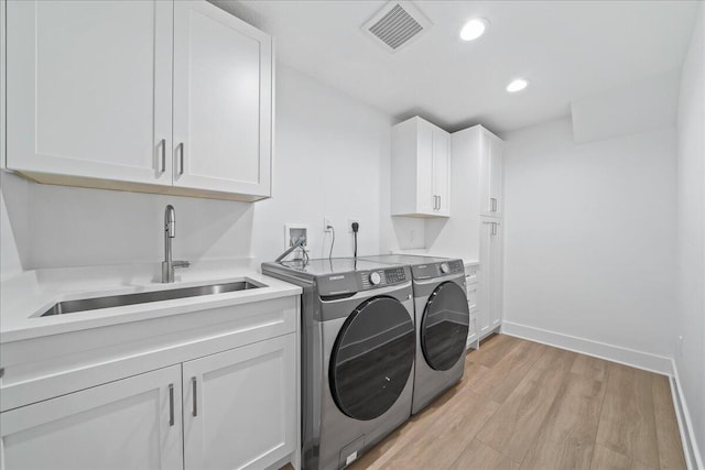 clothes washing area with washer and clothes dryer, cabinets, light wood-type flooring, and sink