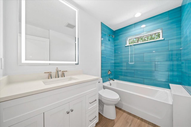 full bathroom featuring wood-type flooring, tiled shower / bath combo, vanity, and toilet