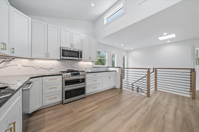 kitchen with white cabinets, stainless steel appliances, decorative backsplash, and light wood finished floors
